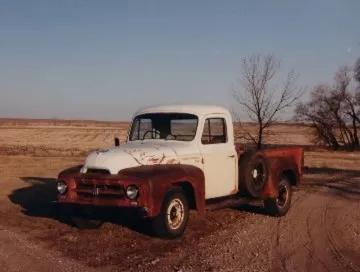 A white truck parked in the dirt near a tree.