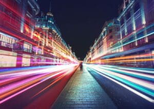 A person is standing on the sidewalk in front of some buildings.