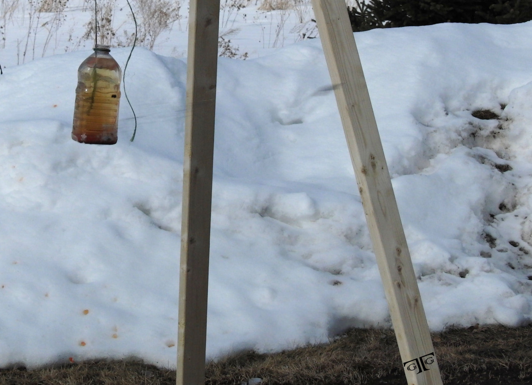 CIMG5880 with GTG Logo - brightened - Cropped A bottle hanging from two wooden poles in the snow.