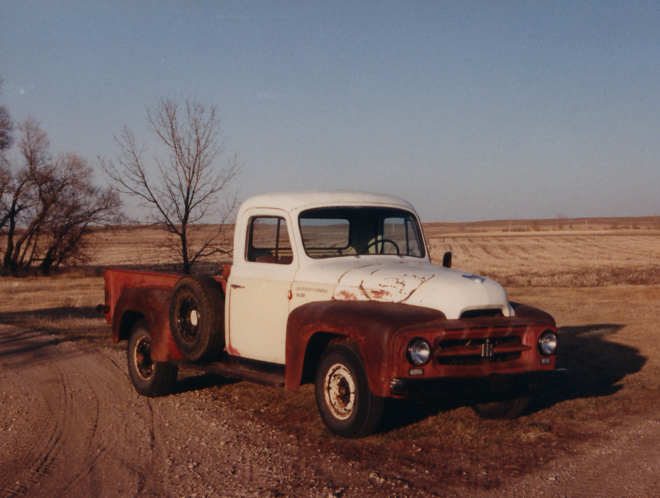 A white truck is parked on the side of a dirt road.